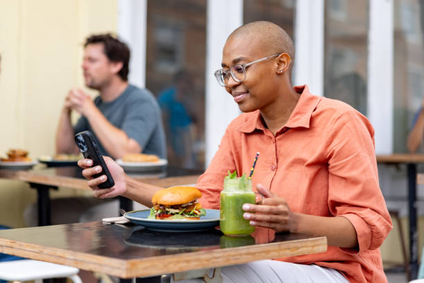 Happy African American woman eating at a restaurant and using her cell phone - lifestyle concepts