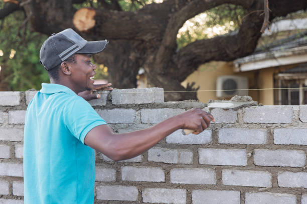 bricklayer african men, using a trowel and a string to align bricks, building a wall at sunset outdoors