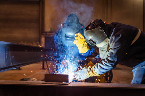 A young university student female is practicing her welding skills while at school under a teacher's supervision.